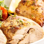 Close-up of juicy, golden-brown air fryer chicken thighs sliced and served with fresh greens and a lemon wedge on a white plate.