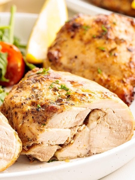Close-up of juicy, golden-brown air fryer chicken thighs sliced and served with fresh greens and a lemon wedge on a white plate.