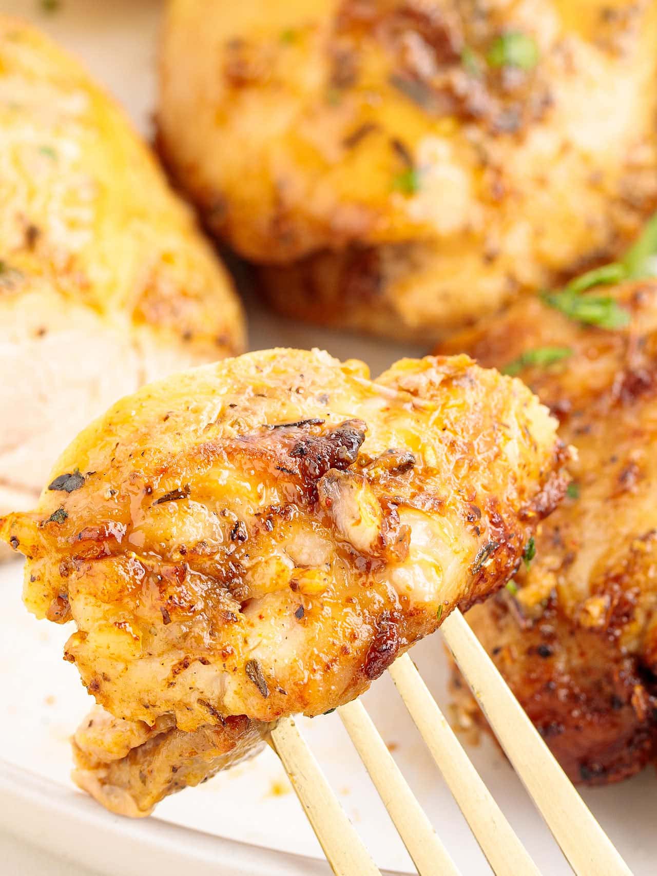 Close-up of a fork holding a juicy, golden air fryer chicken thigh with crispy edges.