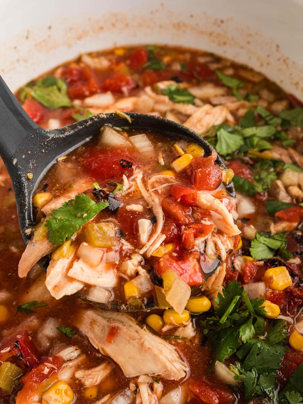 A ladle filled with Chicken Tortilla Soup being removed from a white Crockpot.