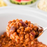 A serving spoon lifting Baked Beans out of a Crock Pot.