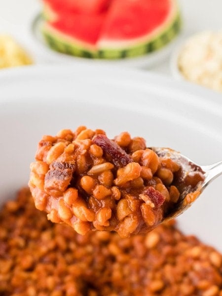 A serving spoon lifting Baked Beans out of a Crock Pot.