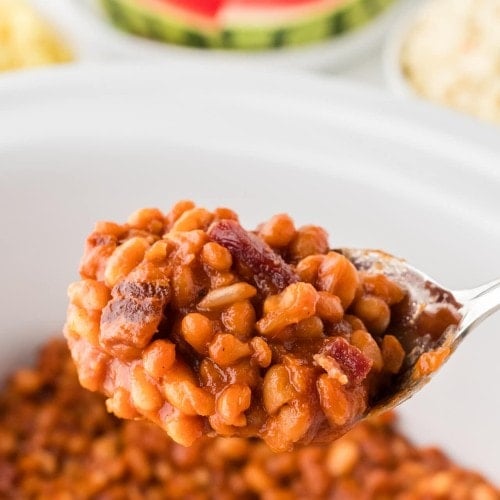 A serving spoon lifting Baked Beans out of a Crock Pot.