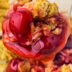 A spoon full of cherry pie is being held up.
