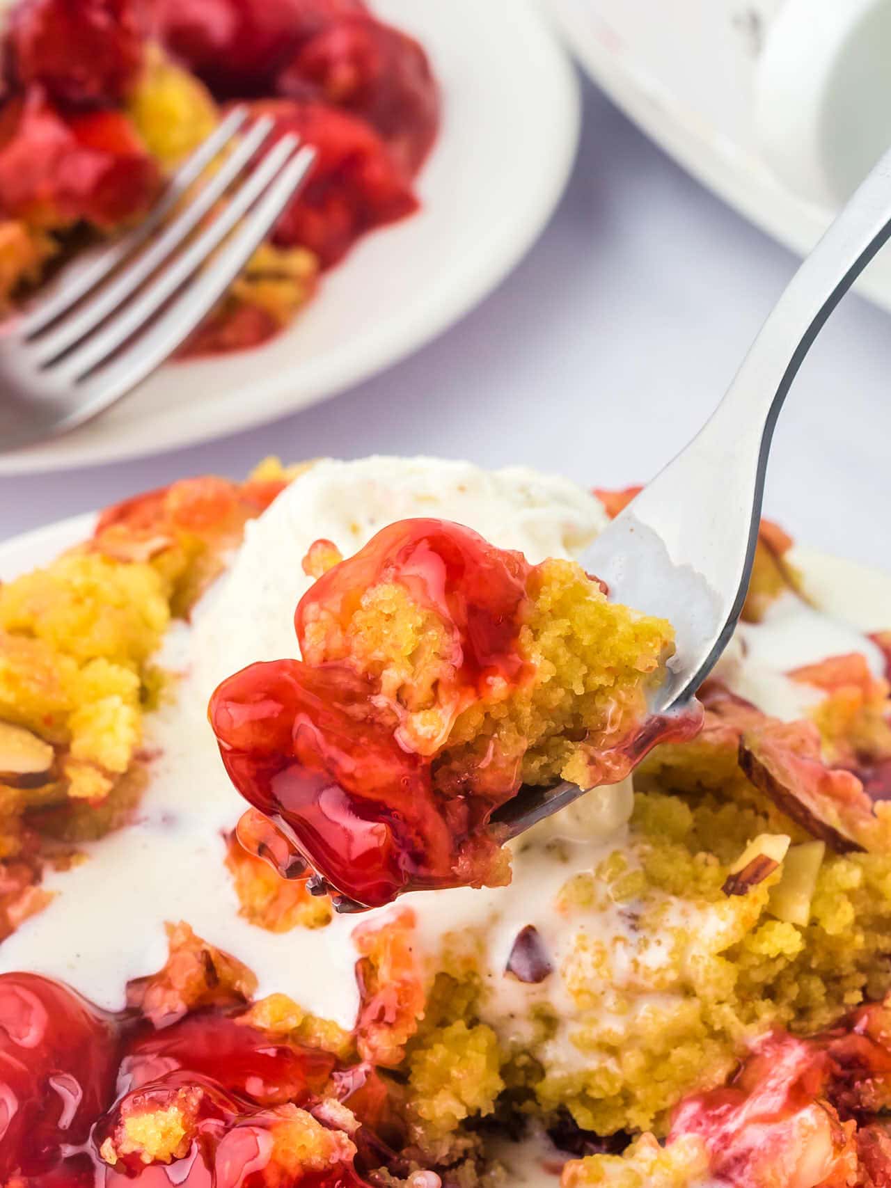 A spoon is lifting a piece of Crock Pot Cherry Dump Cake from a plate.