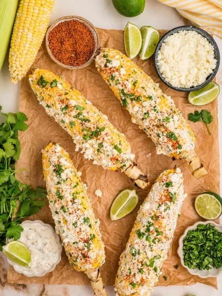 Top down view of Elote served with extra cheese, lime wedges, and cilantro.