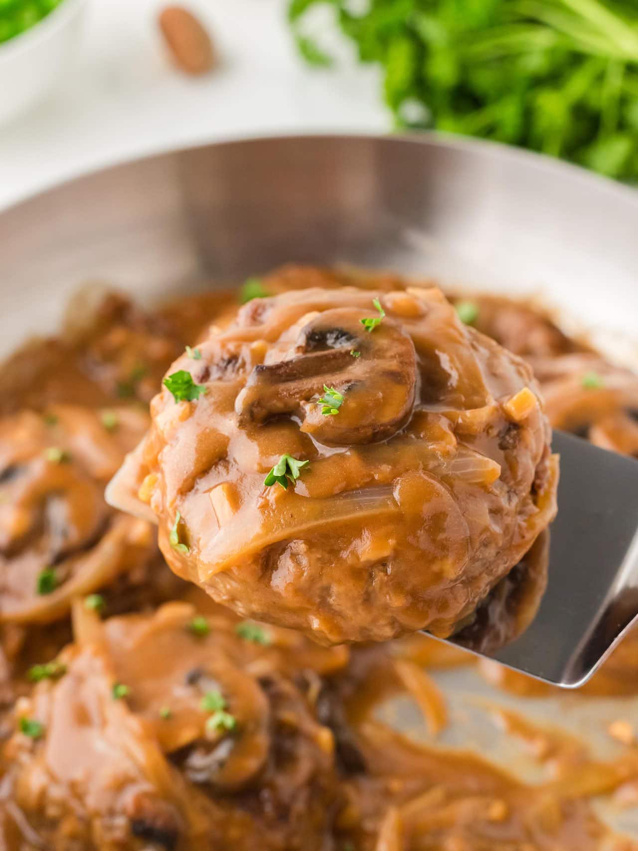 Lifting a Salisbury Steak with a spatula out of a skillet.