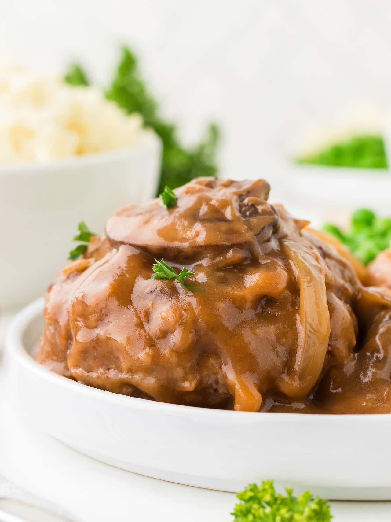 Salisbury Steak served on a white plate with mashed potatoes and peas.