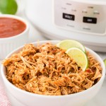 A bowl of Slow Cooker Salsa Chicken served in a white bowl with slices of lime.