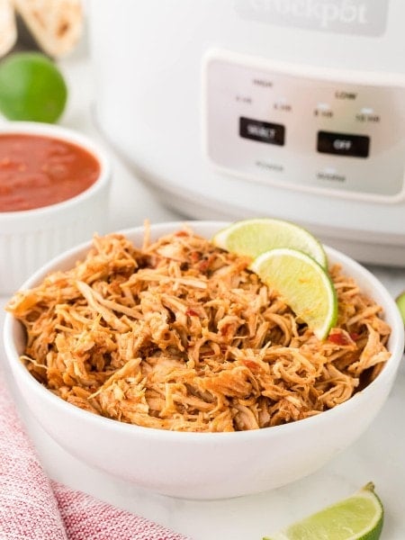 A bowl of Slow Cooker Salsa Chicken served in a white bowl with slices of lime.