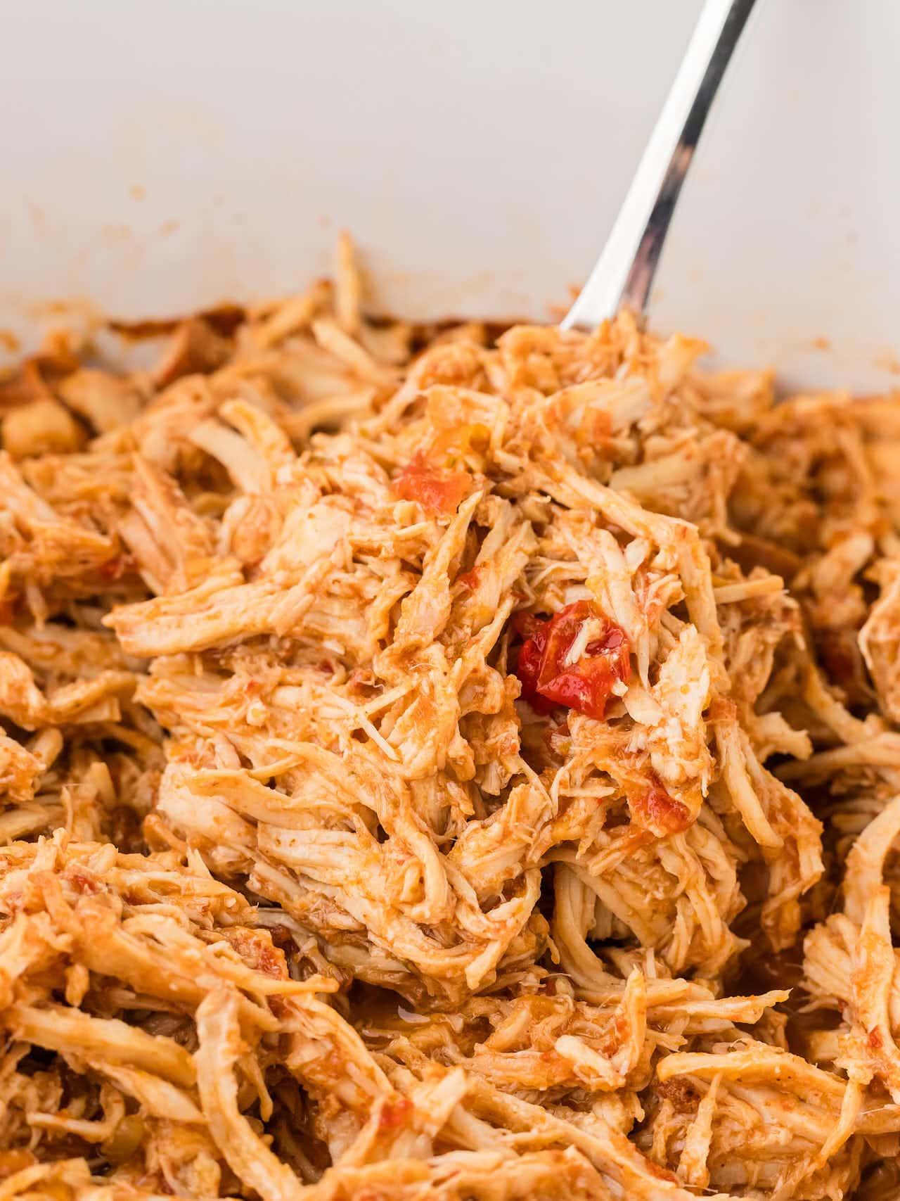 A serving fork lifting tender Chicken Salsa out of a slow cooker.