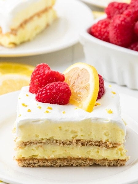 Lemon Icebox Cake topped with raspberries and lemon slices on a white plate.