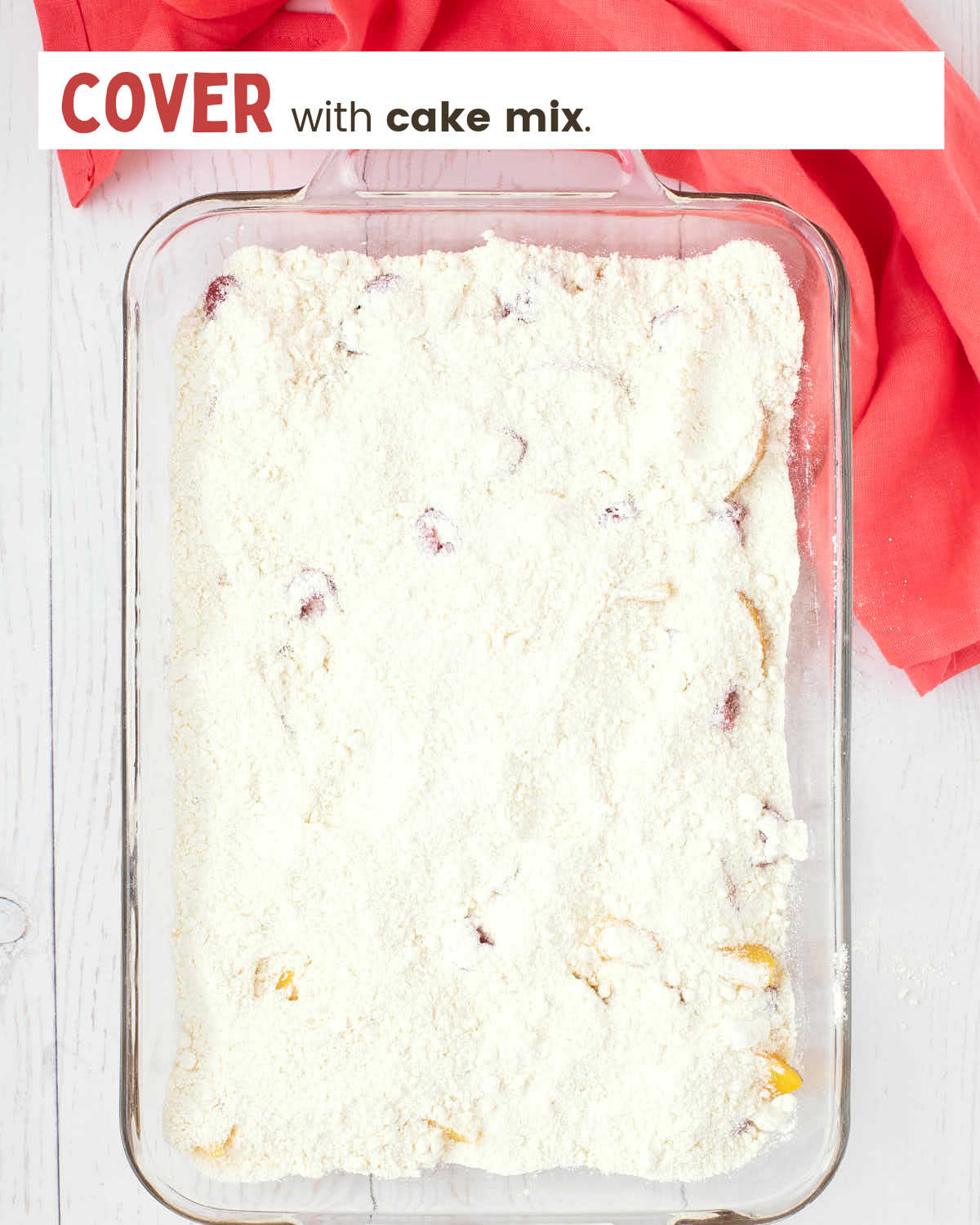 Peach slices and raspberries topped with cake mix in a 9x13" glass dish.