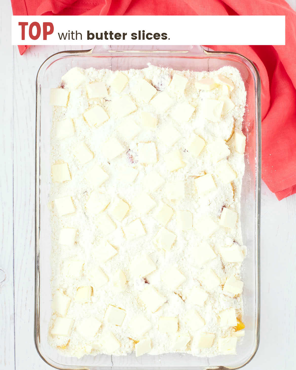 Peach slices and raspberries topped with cake mix and butter slices in a 9x13" glass dish.