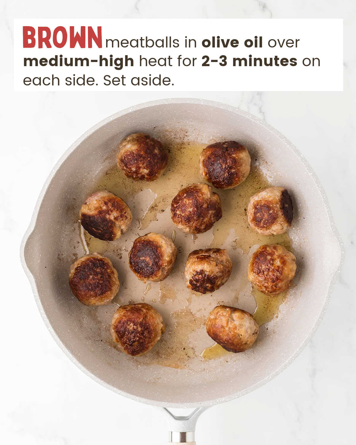 Browned meatballs in olive oil in a skillet.