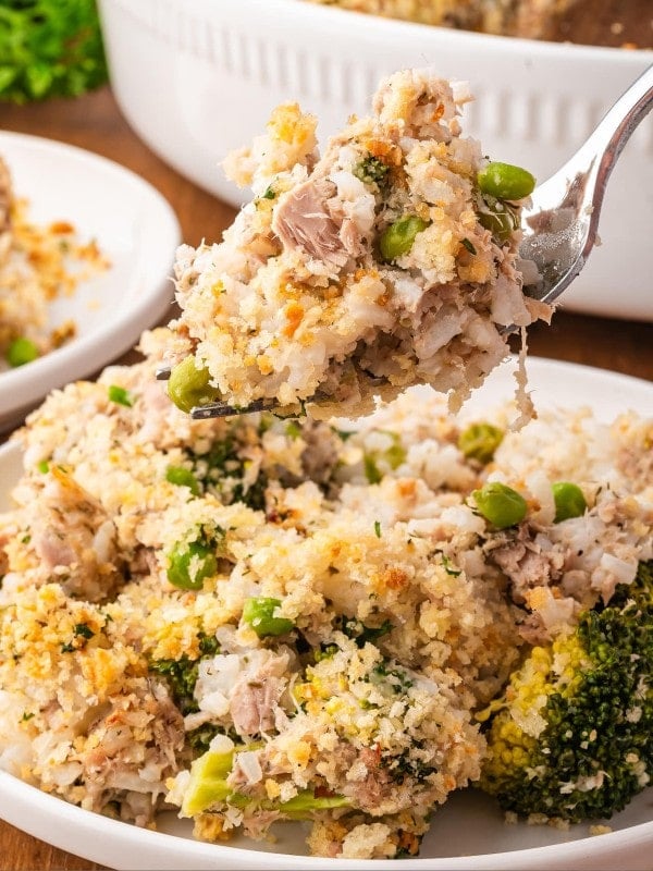 A forkful of Tuna Rice Casserole that's served on a white plate.