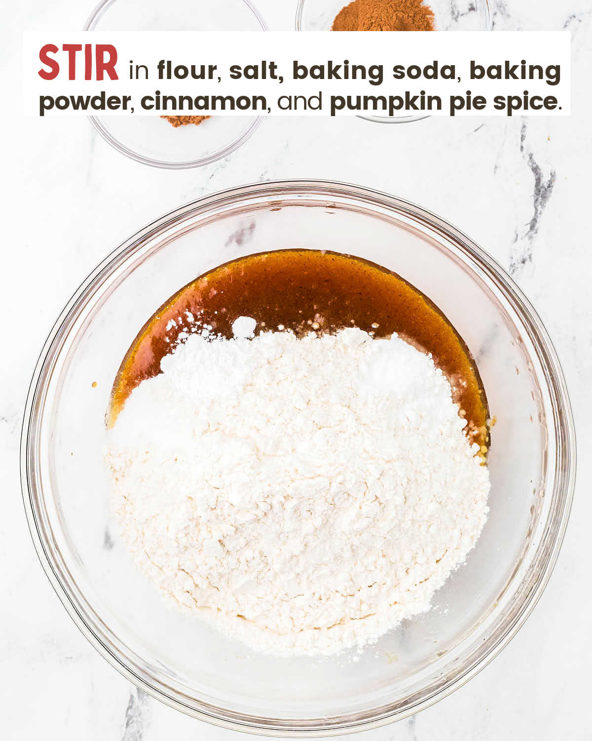 Whisked brown butter mixture topped with flour and other dry ingredients in a glass bowl.