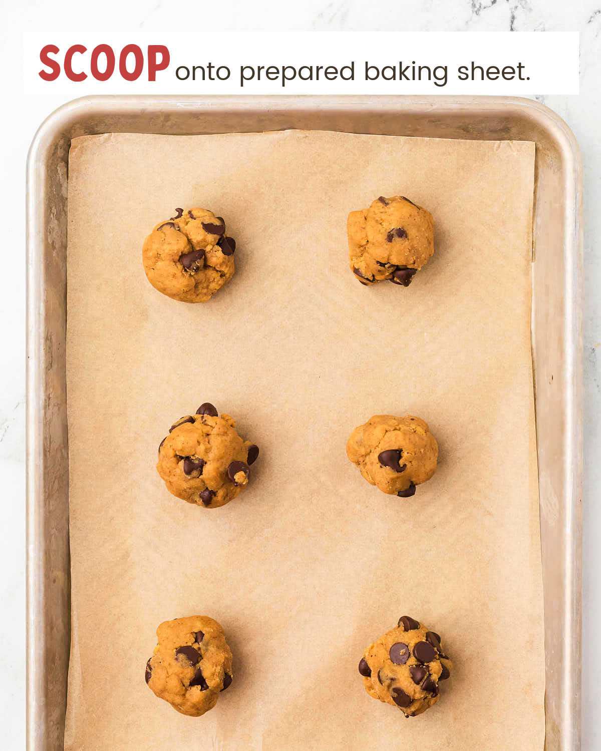 Chocolate Chip Pumpkin cookie dough in scoops on a baking tray lined with parchment paper.