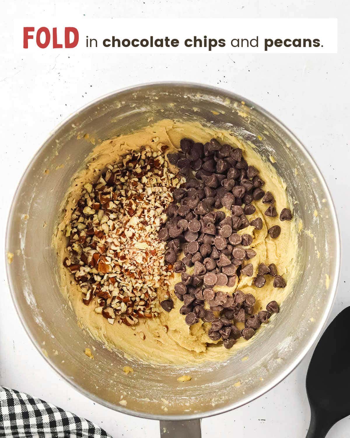 Cookie batter with chopped pecans and chocolate chips on top in a metal mixing bowl.