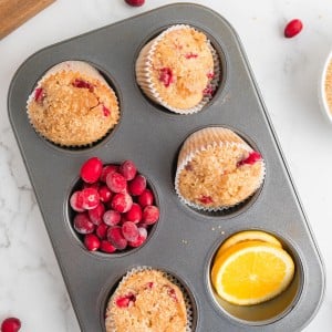 Topdown view of Cranberry Orange Muffins in a muffin tins decorated with orange slices and fresh cranberries.
