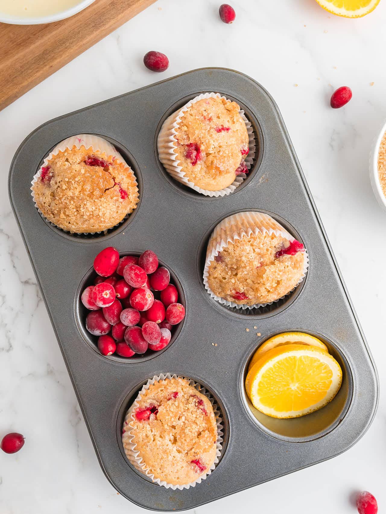 Topdown view of Cranberry Orange Muffins in a muffin tins decorated with orange slices and fresh cranberries.