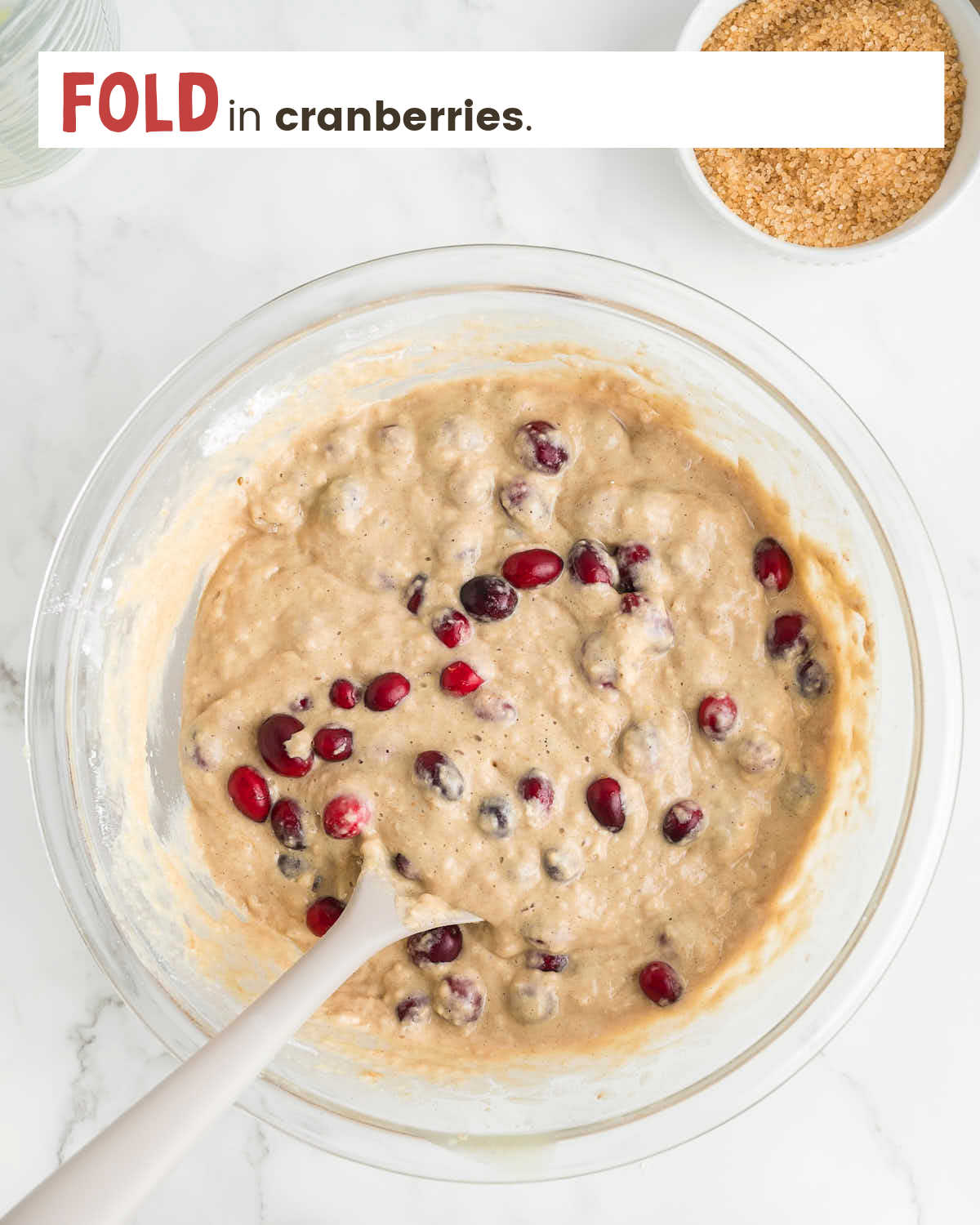 A wooden spoon folds cranberries into muffin batter.