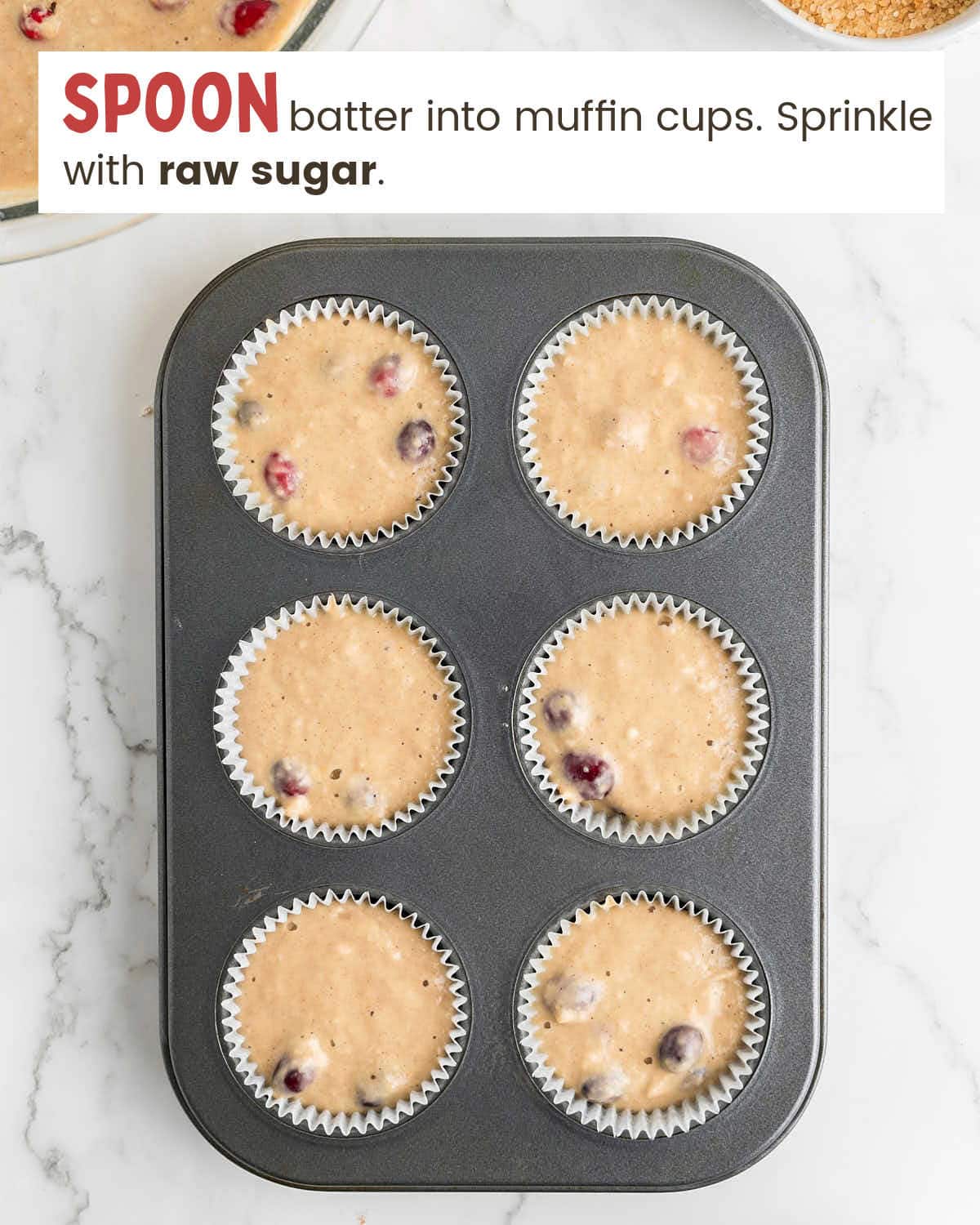 Cranberry orange muffin batter in muffin cups in a muffin tin.