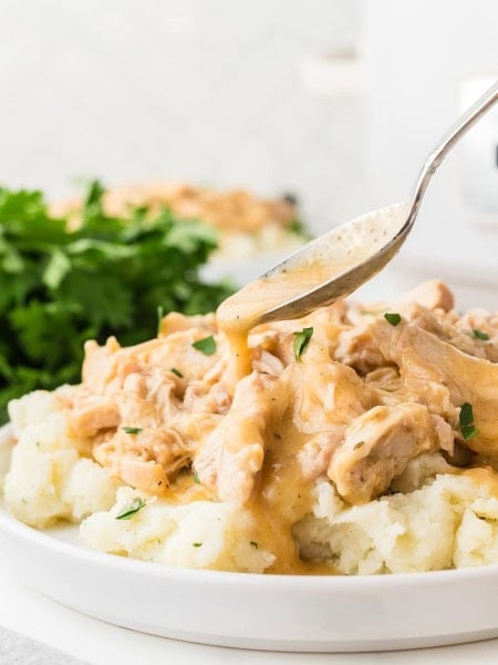 Drizzling gravy over Crockpot Chicken and Gravy served over mashed potatoes.