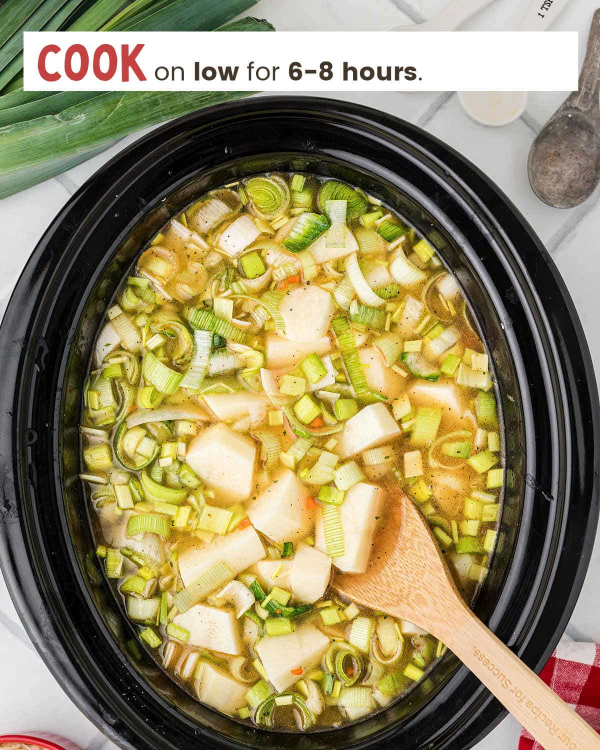 A wooden spoon in potato and leek soup in a slow cooker.