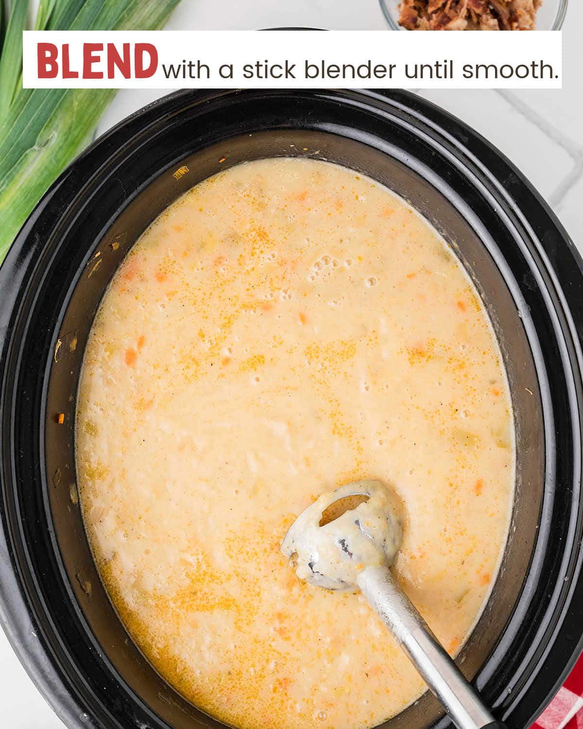A stick blender in a slow cooker with potato and leek soup.