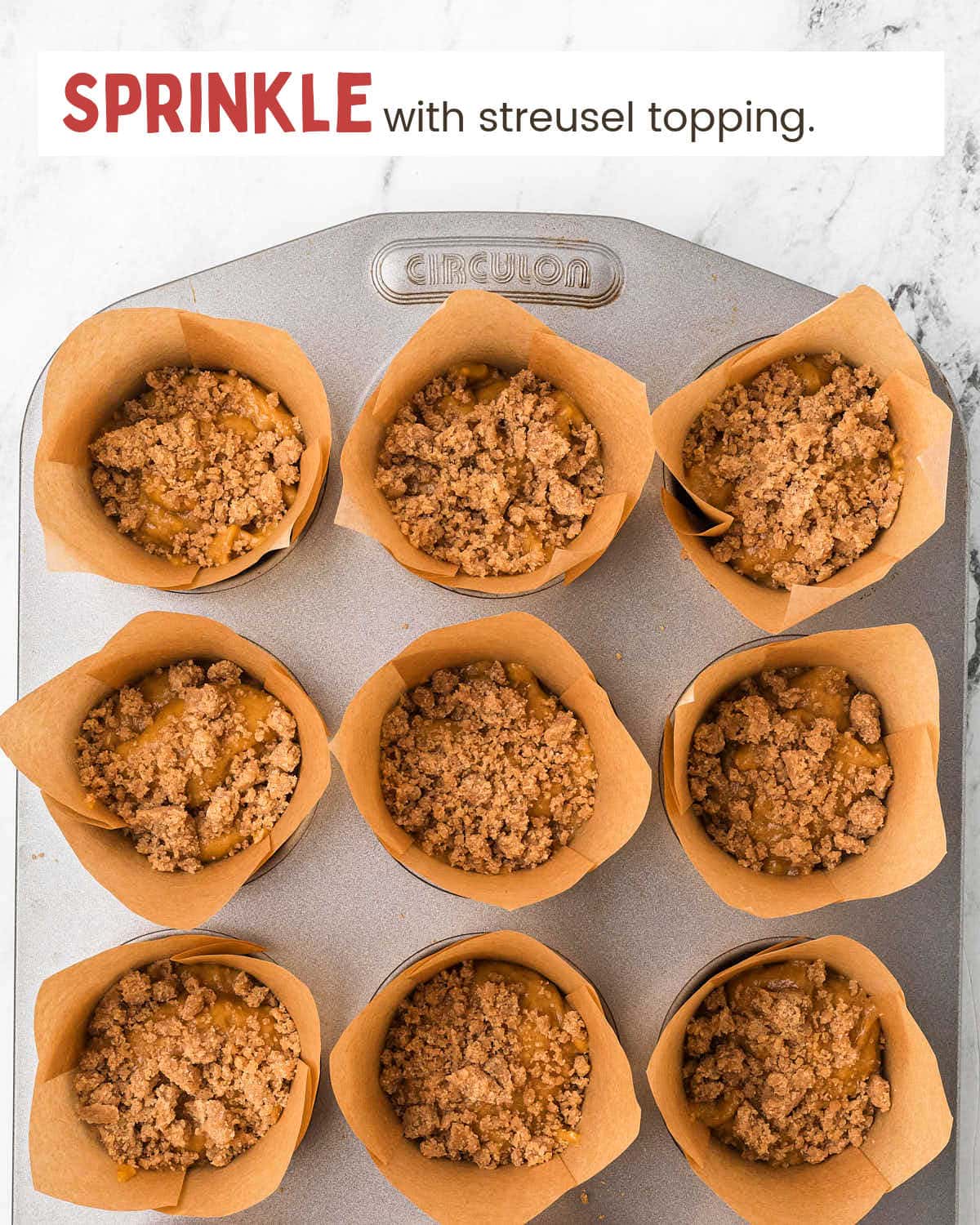 Pumpkin muffin batter topped with streusel in muffin tin cups lined with parchment paper.