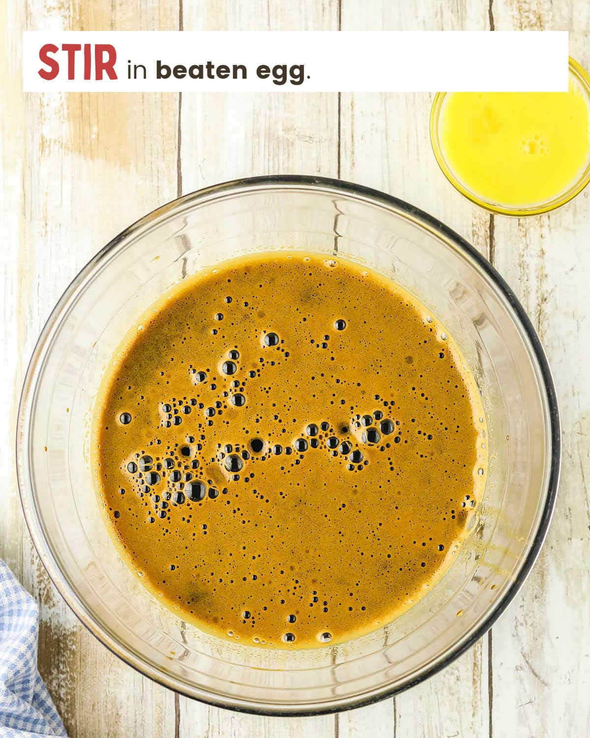 Molasses, hot water, and baking soda in a glass bowl with a beaten egg in a small dish.
