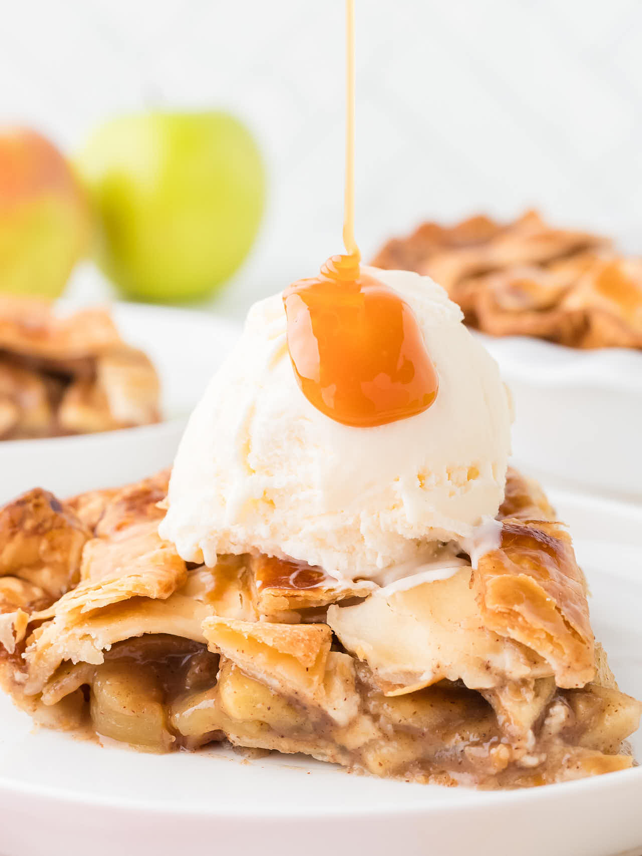 A slice of Apple Pie with a scoop of vanilla ice cream drizzled with caramel sauce.