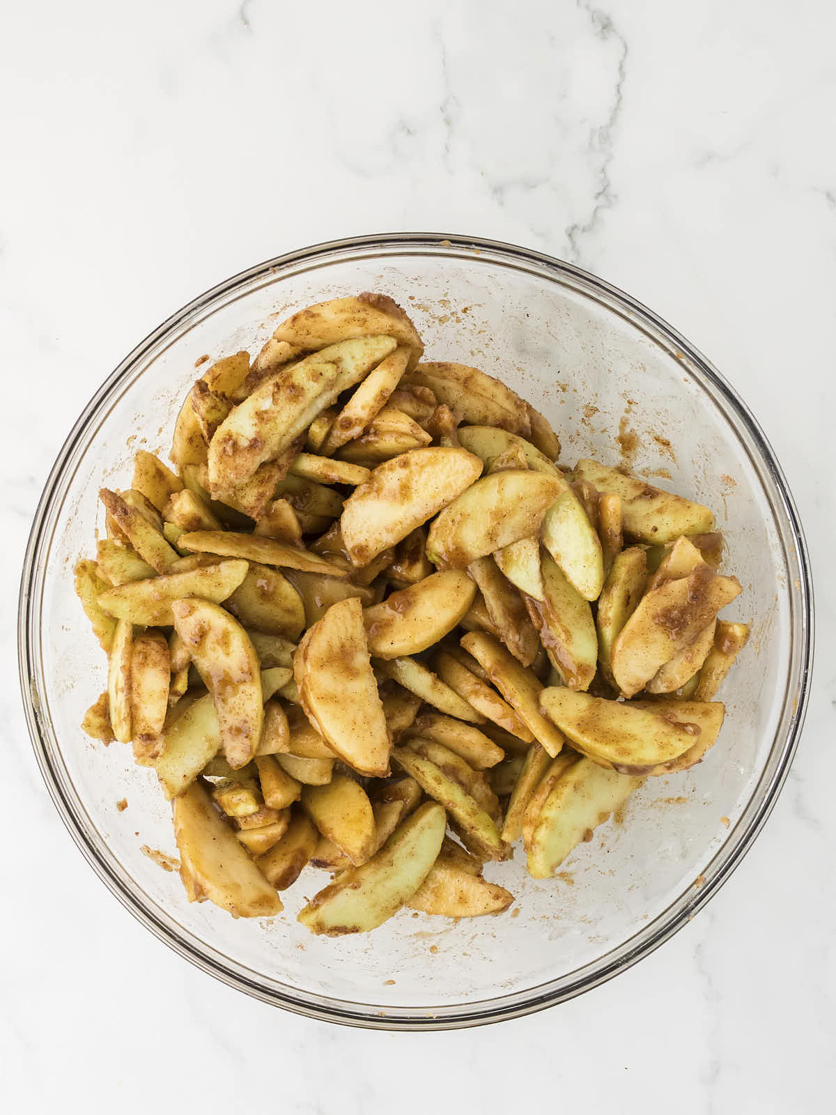 Seasoned apple slices in a glass bowl.