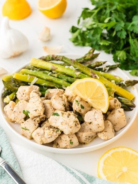 A plate of Garlic Butter Chicken Bites served with roasted asparagus and a fresh lemon wedge.
