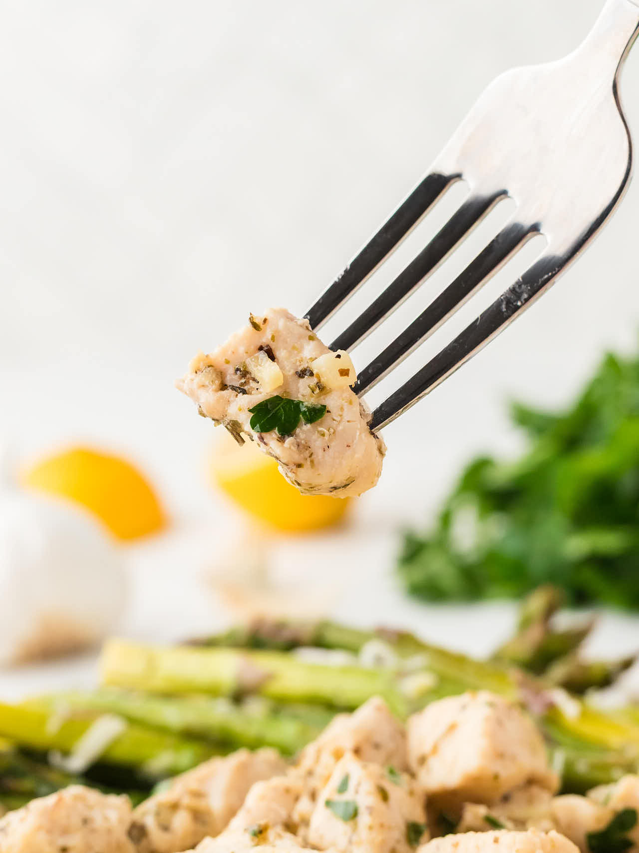 A forkful of Garlic Butter Chicken Bites held up close, with asparagus blurred behind.