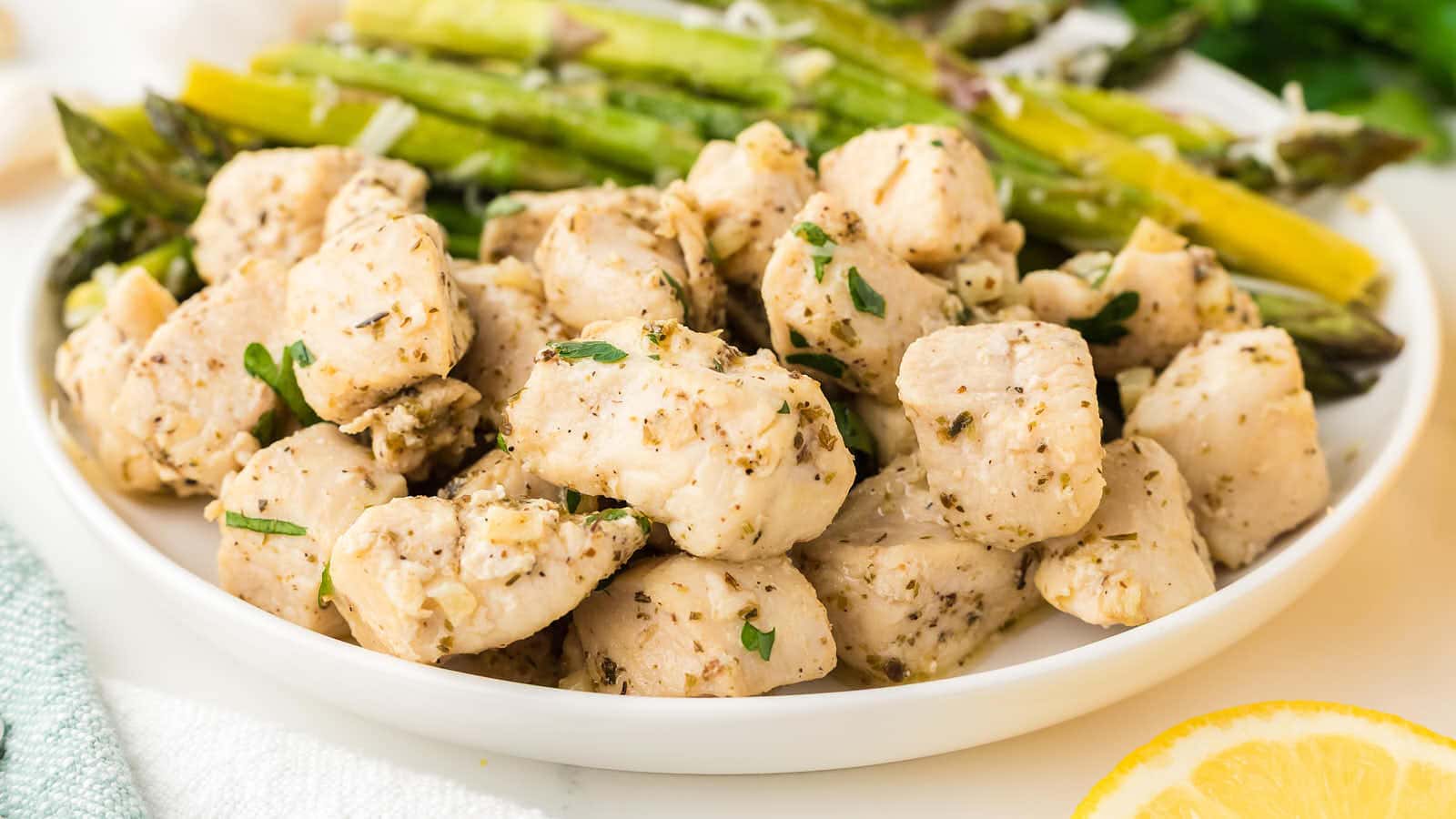 Close-up of Garlic Butter Chicken Bites on a white plate with roasted asparagus.