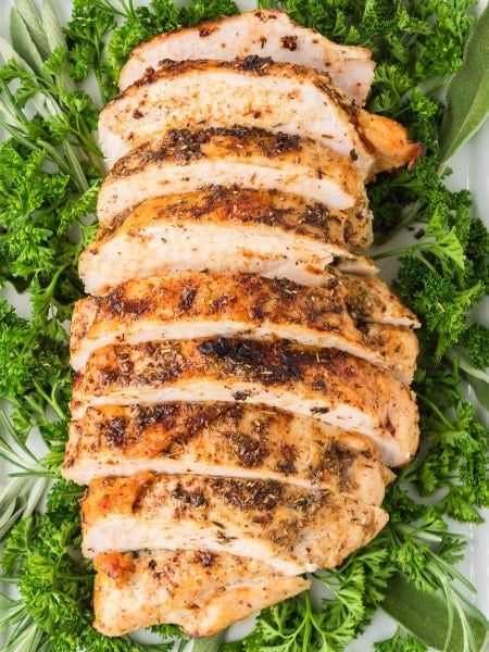 Juicy Roasted Turkey sliced and arranged on a platter with fresh parsley and herbs.