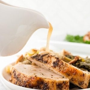 Juicy Roasted Turkey Breast slices on a plate with gravy being poured from a white gravy boat.