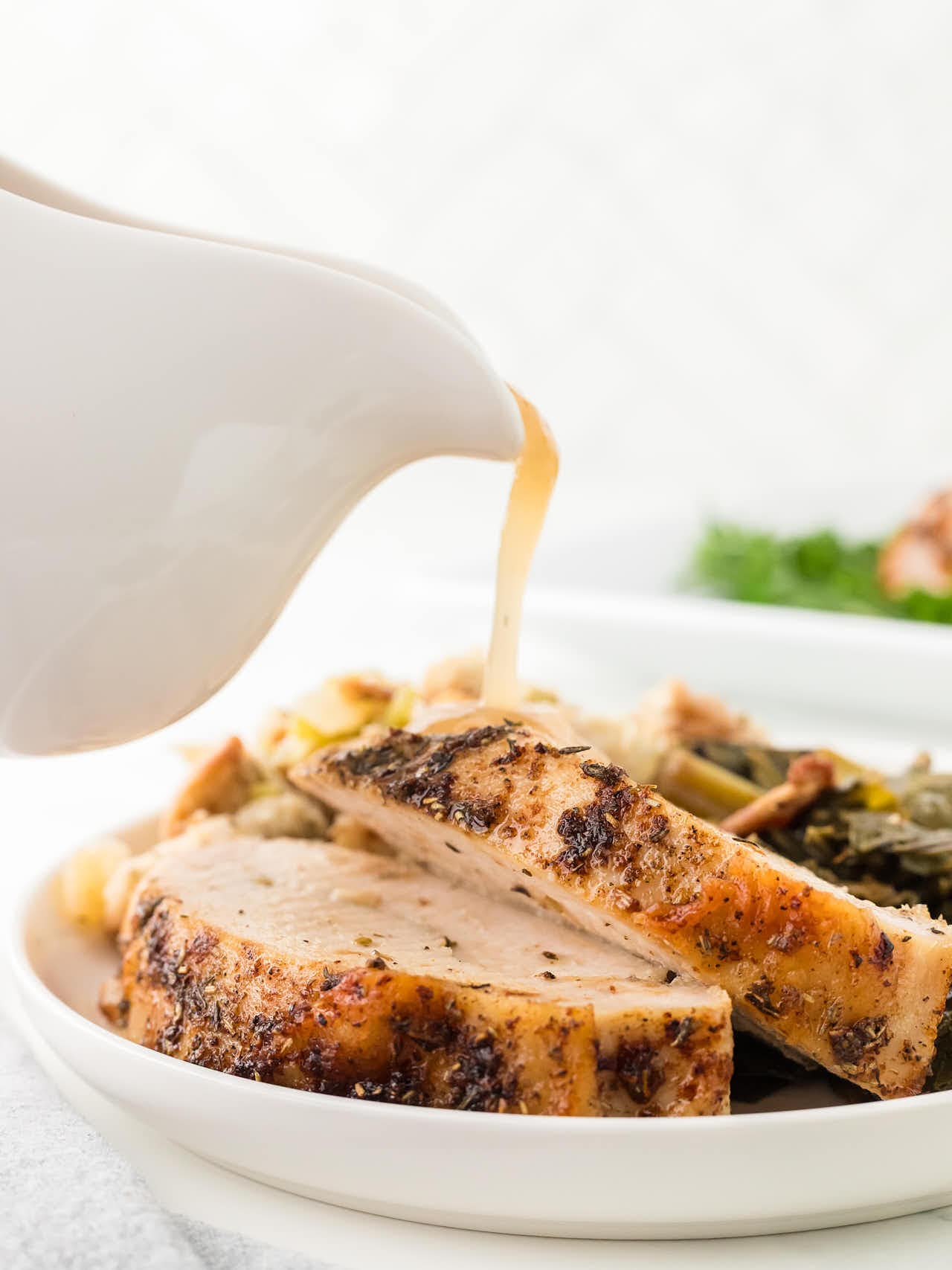Juicy Roasted Turkey Breast slices on a plate with gravy being poured from a white gravy boat.