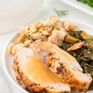 Juicy Roasted Turkey slices topped with gravy, served with stuffing and collard greens on a white plate.