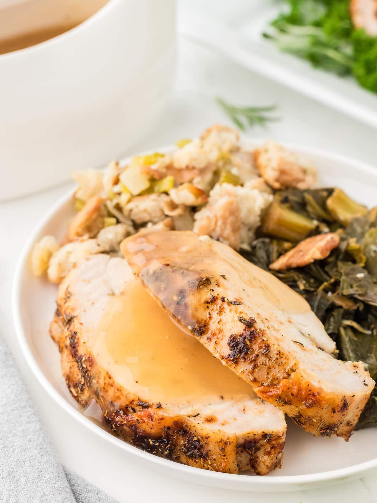 Juicy Roasted Turkey slices topped with gravy, served with stuffing and collard greens on a white plate.