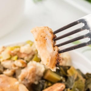 Fork holding a tender bite of Roasted Turkey Breast with stuffing and collard greens in the background.