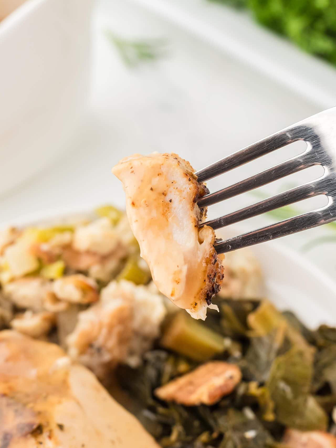 Fork holding a tender bite of Roasted Turkey Breast with stuffing and collard greens in the background.