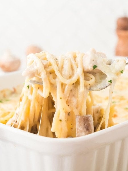 Cheesy Turkey Tetrazzini with spaghetti noodles, mushrooms, and creamy sauce lifted from a white baking dish.