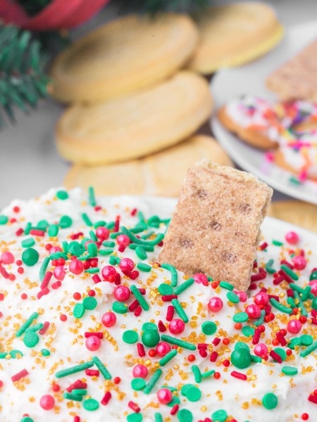 Christmas Dip topped with red, green, and gold sprinkles, served with graham crackers and sugar cookies in the background.