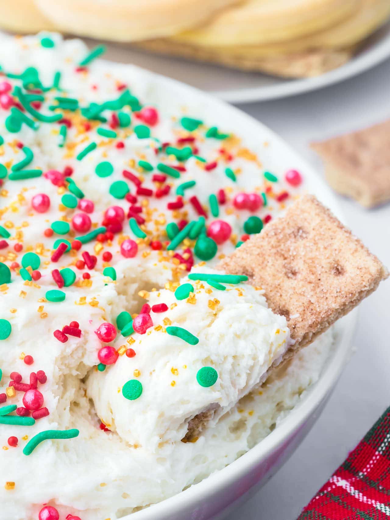Bowl of fluffy Christmas Dip decorated with red, green, and gold sprinkles, served with a graham cracker for dipping.