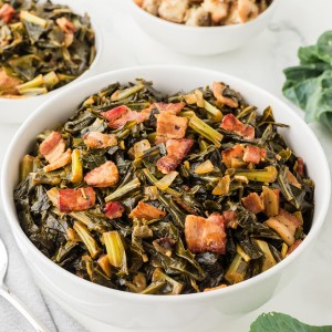 Bowl of Southern-style Collard Greens cooked with bacon and onions on a white marble table, served alongside stuffing and turkey.