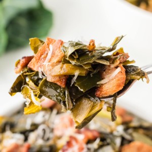 Close up of tender collard greens with crispy bacon and onions lifted on a spoon, showing savory texture and flavor.