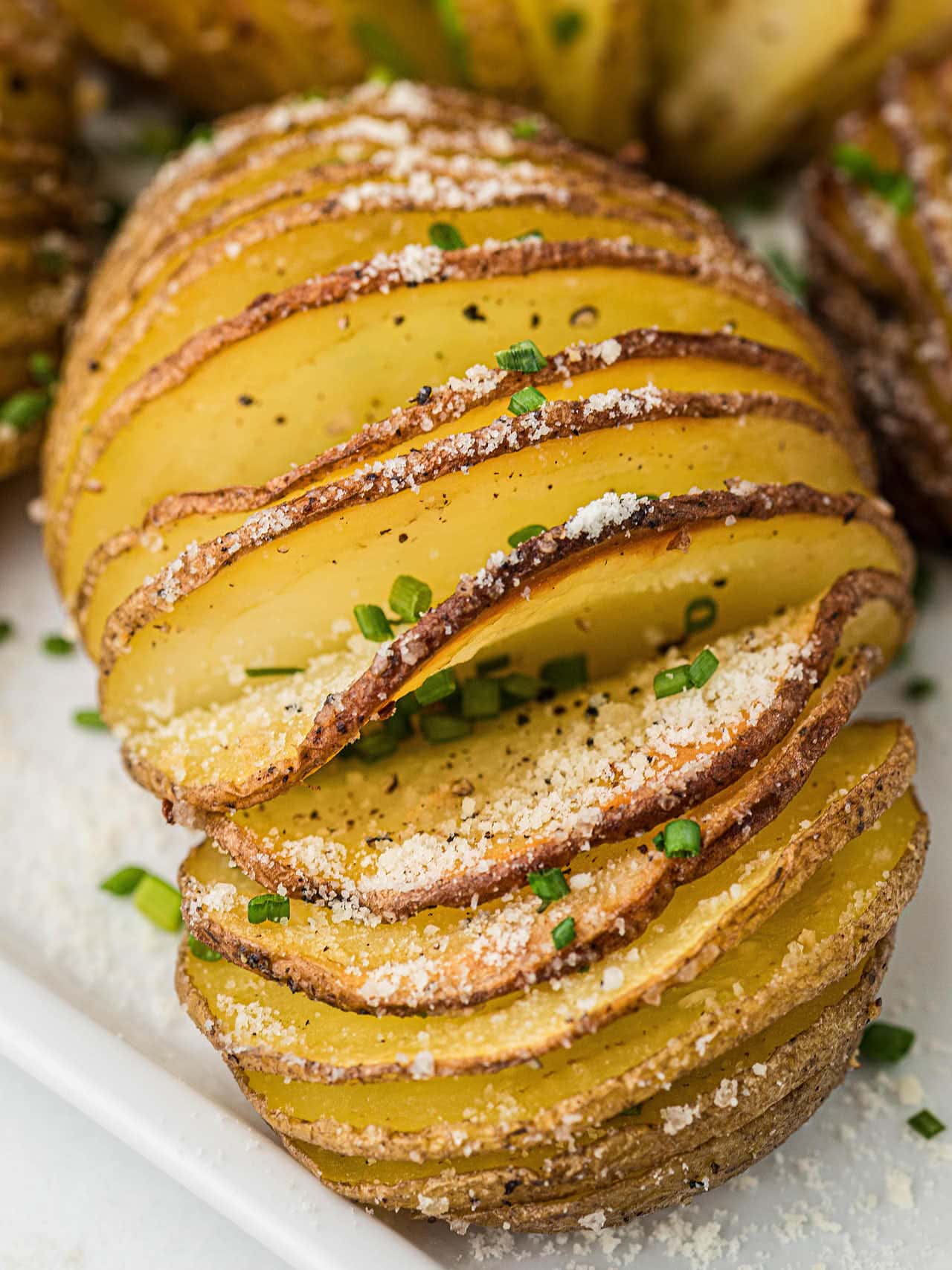 Closeup of a Hasselback Potato on a white plate.